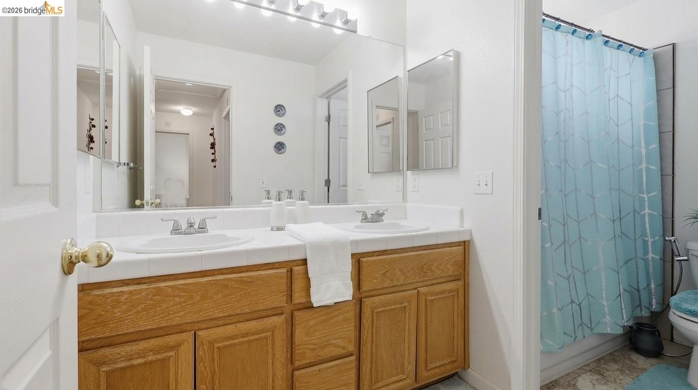 Bathroom with an oak double vanity, mirrored cabinets, and a blue patterned shower curtain.