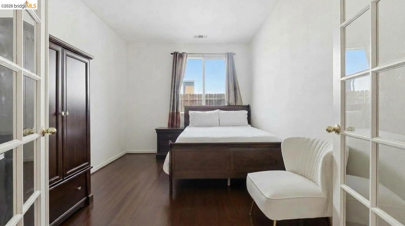 Bedroom with dark wood furniture, hardwood floors, and a white upholstered chair beside the bed.