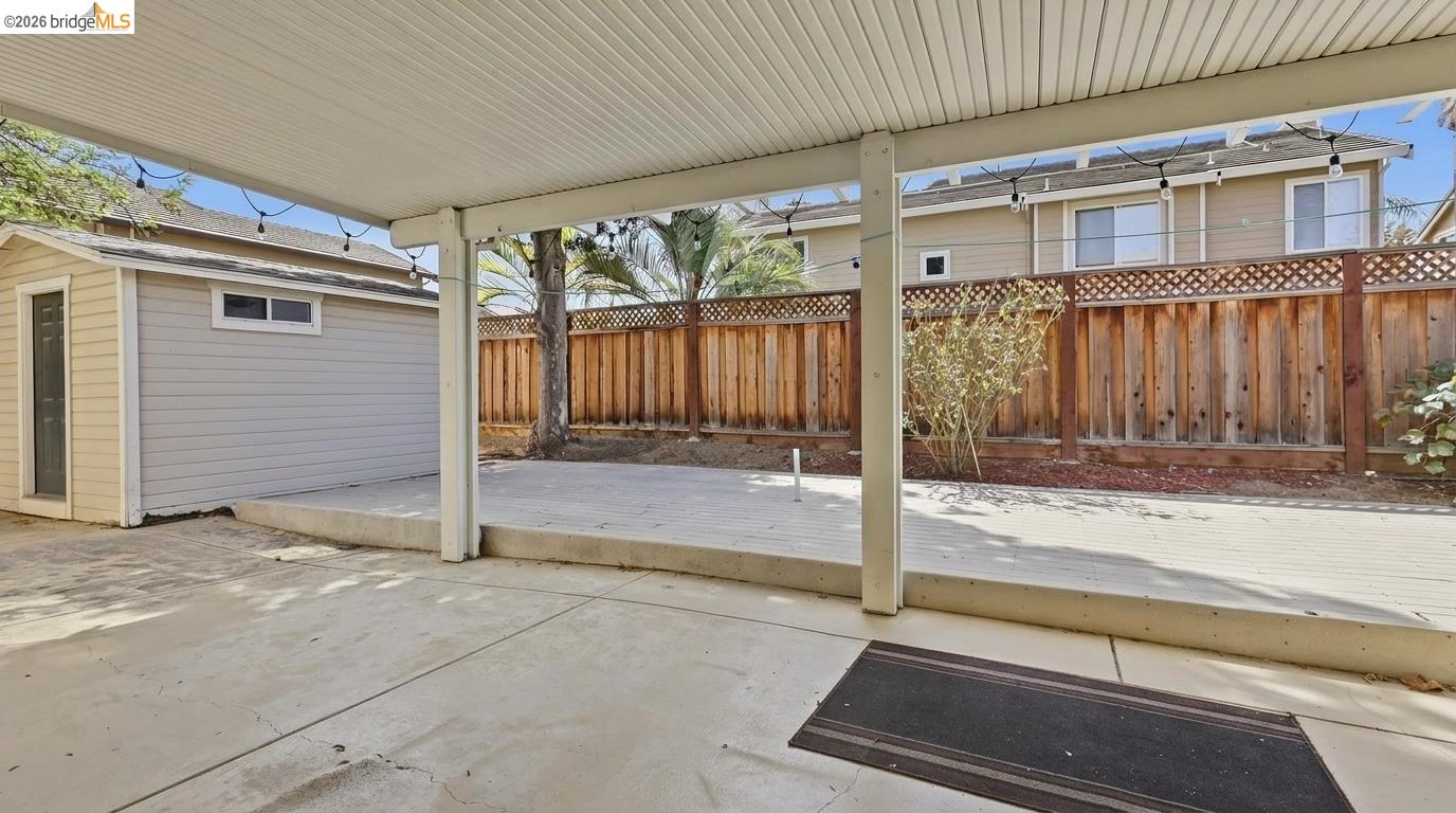 Covered backyard patio with a raised deck, shed, and tall wooden fence.