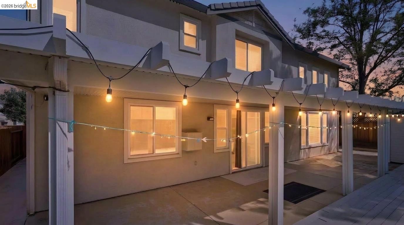 Two-story home’s rear patio at dusk, illuminated by warm string lights and glowing windows.