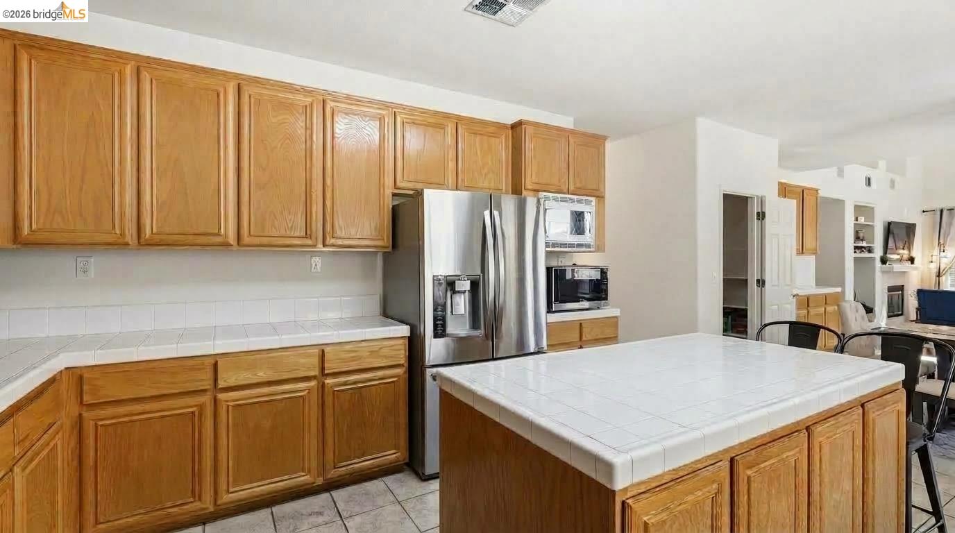 Kitchen with honey-colored cabinets, a large white-tile island, and stainless steel appliances.