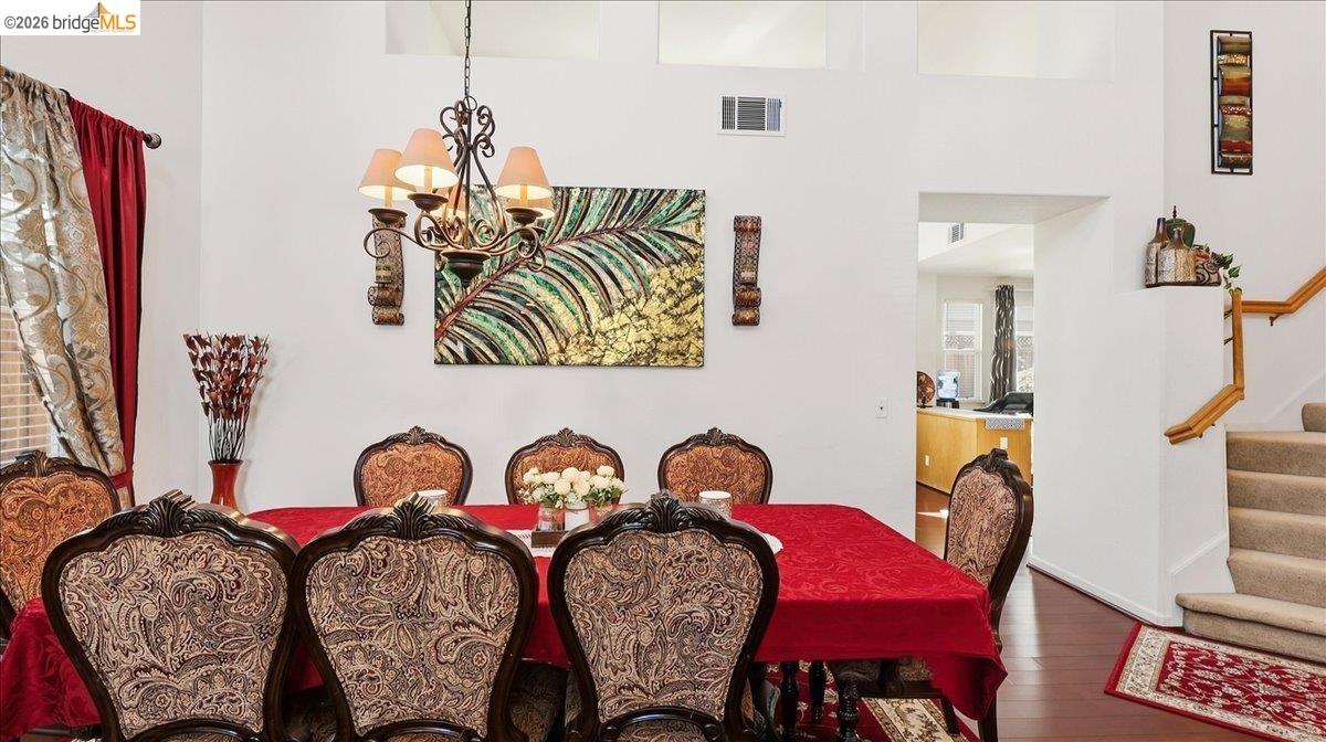 Dining room with ornate patterned chairs, a red tablecloth, chandelier, and stairs beside the kitchen doorway.