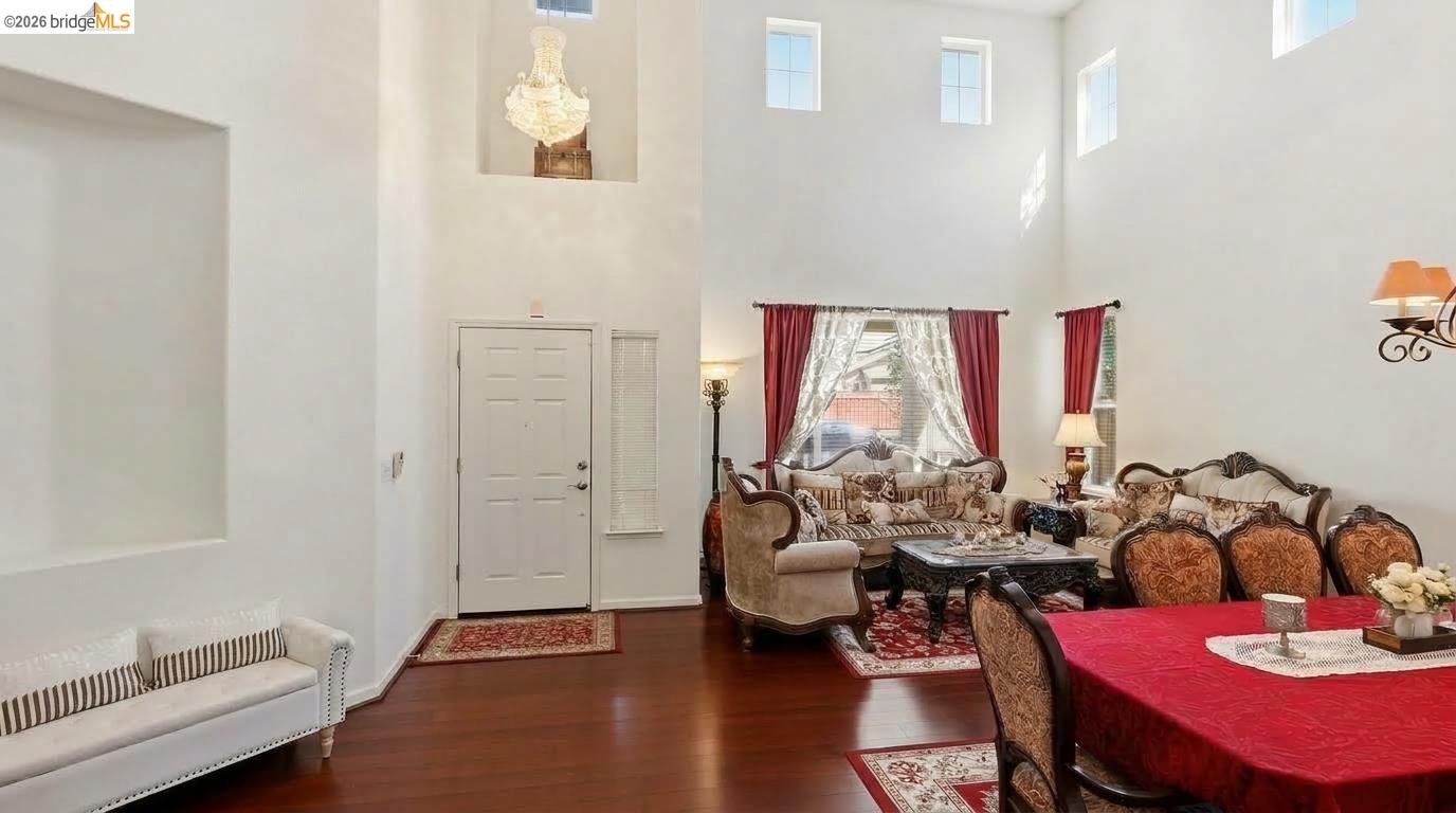 Living and dining room with soaring ceilings, dark hardwood floors, and an ornate chandelier.