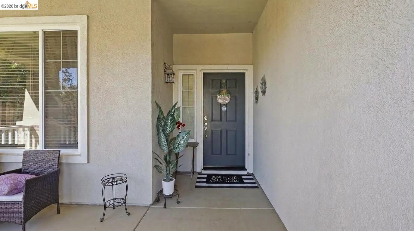 Covered front porch with a dark blue entry door, potted plant, and seating beside the window.