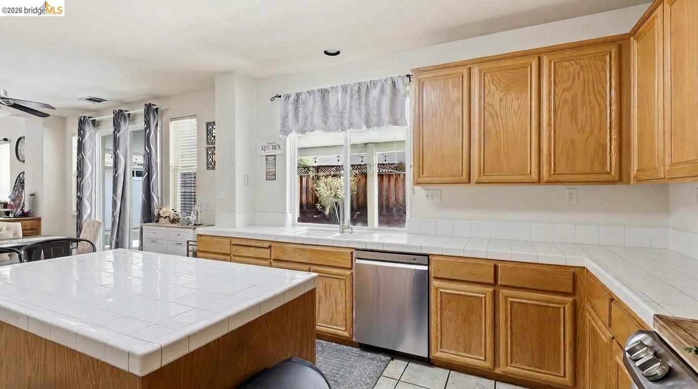 Kitchen with honey-colored wood cabinets, white tile countertops, a large island, and stainless steel dishwasher.