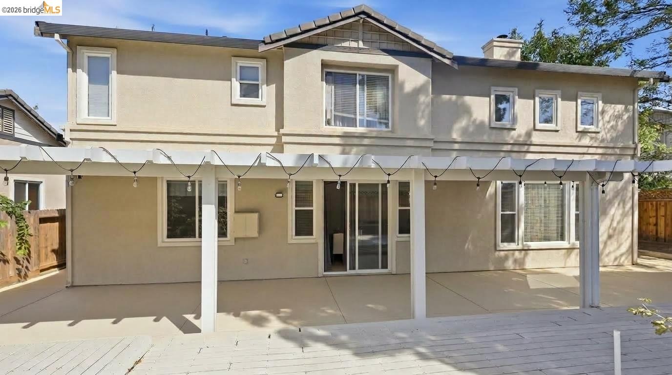 Two-story beige house with a covered patio, string lights, and a wooden deck.