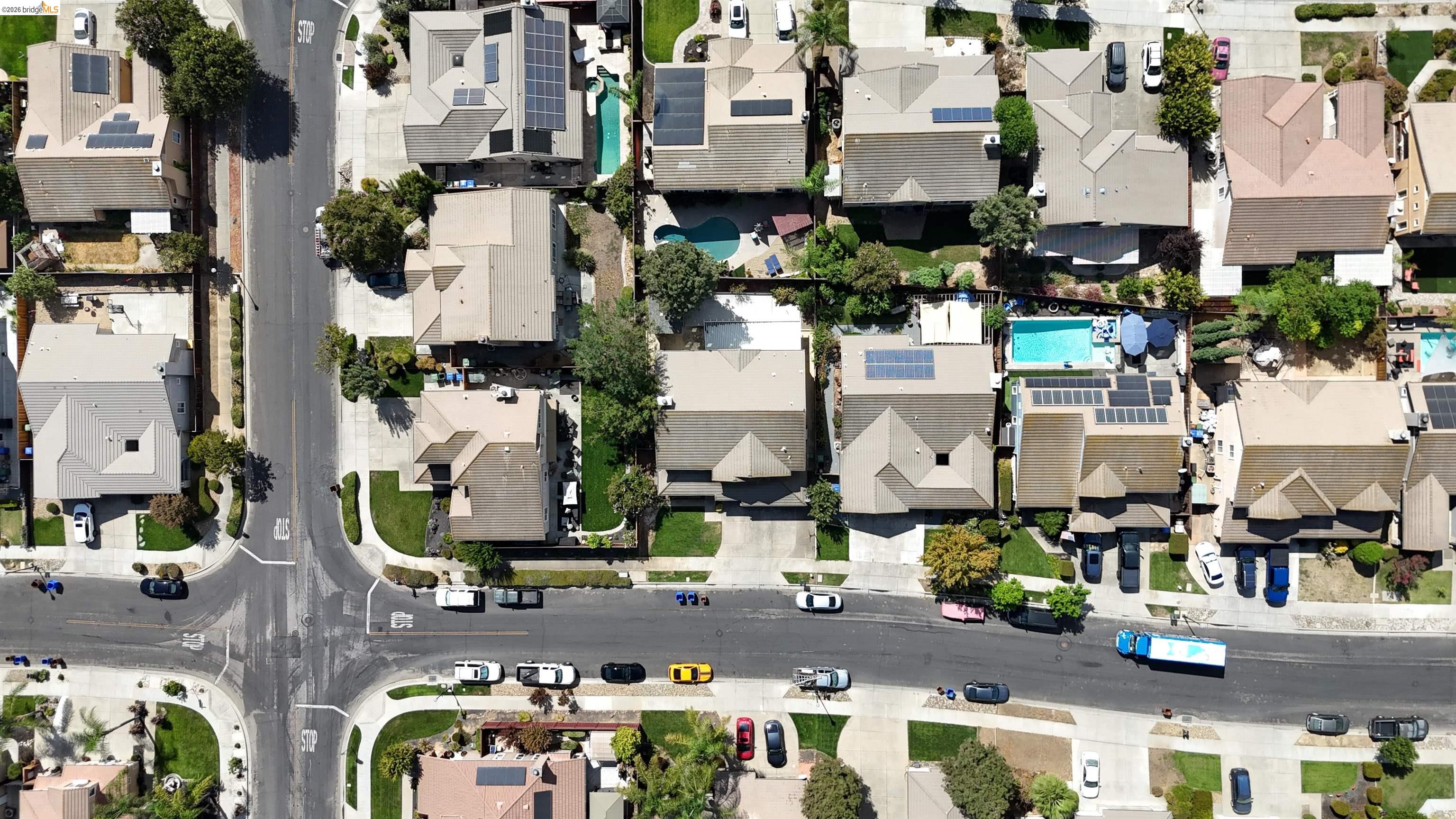 Aerial neighborhood view with homes, rooftop solar panels, and backyard swimming pools.