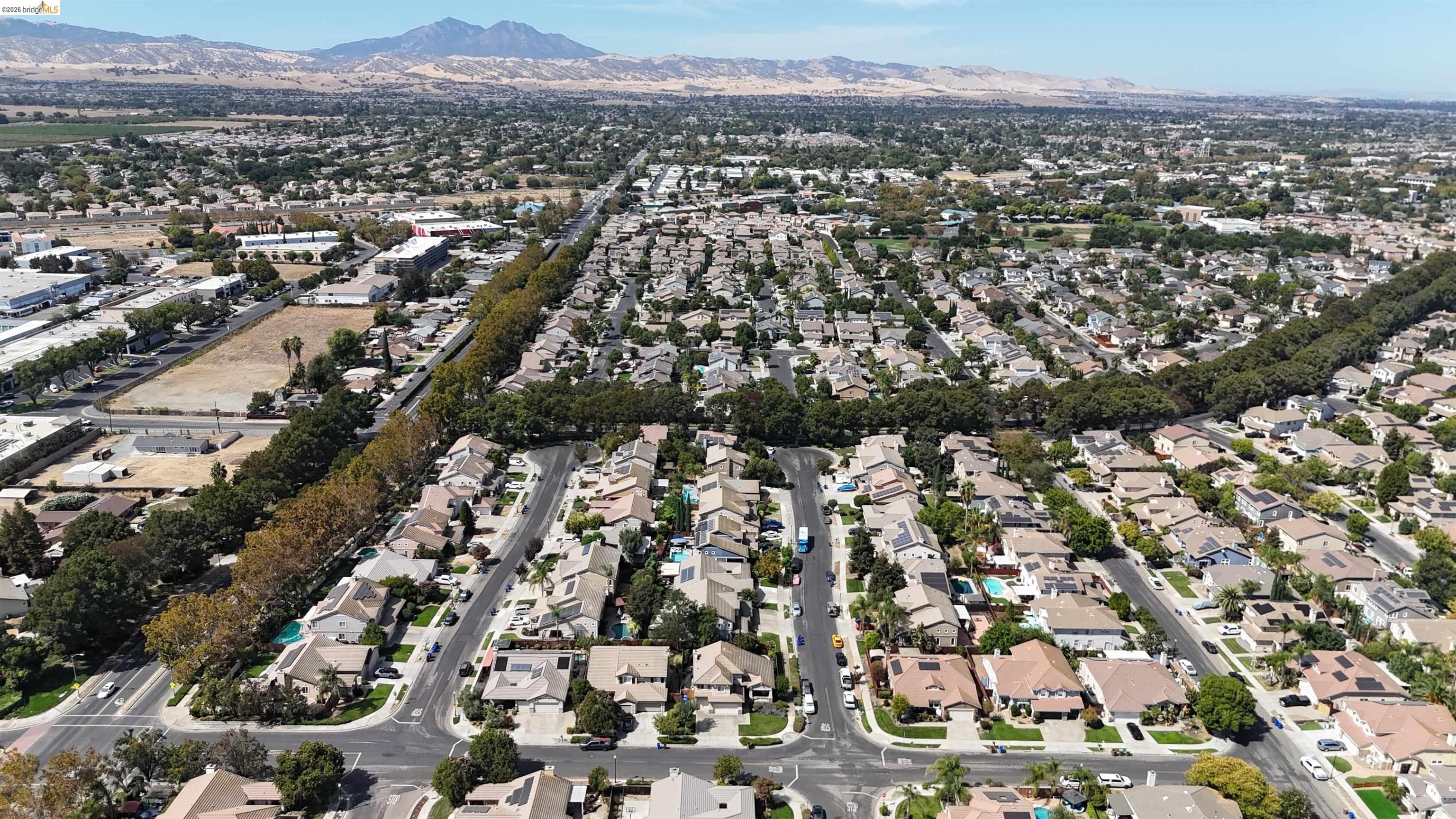 Aerial neighborhood view with tree-lined streets and a mountain range beyond the homes.
