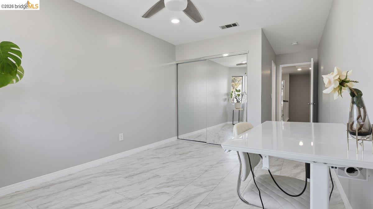 Bright bedroom with mirrored closet doors, marble-look tile floors, and a ceiling fan.