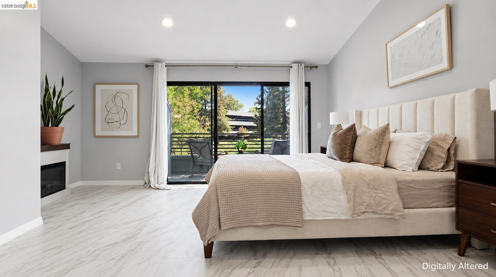 Staged bedroom with a large upholstered bed, fireplace, and sliding doors to a tree-lined balcony.