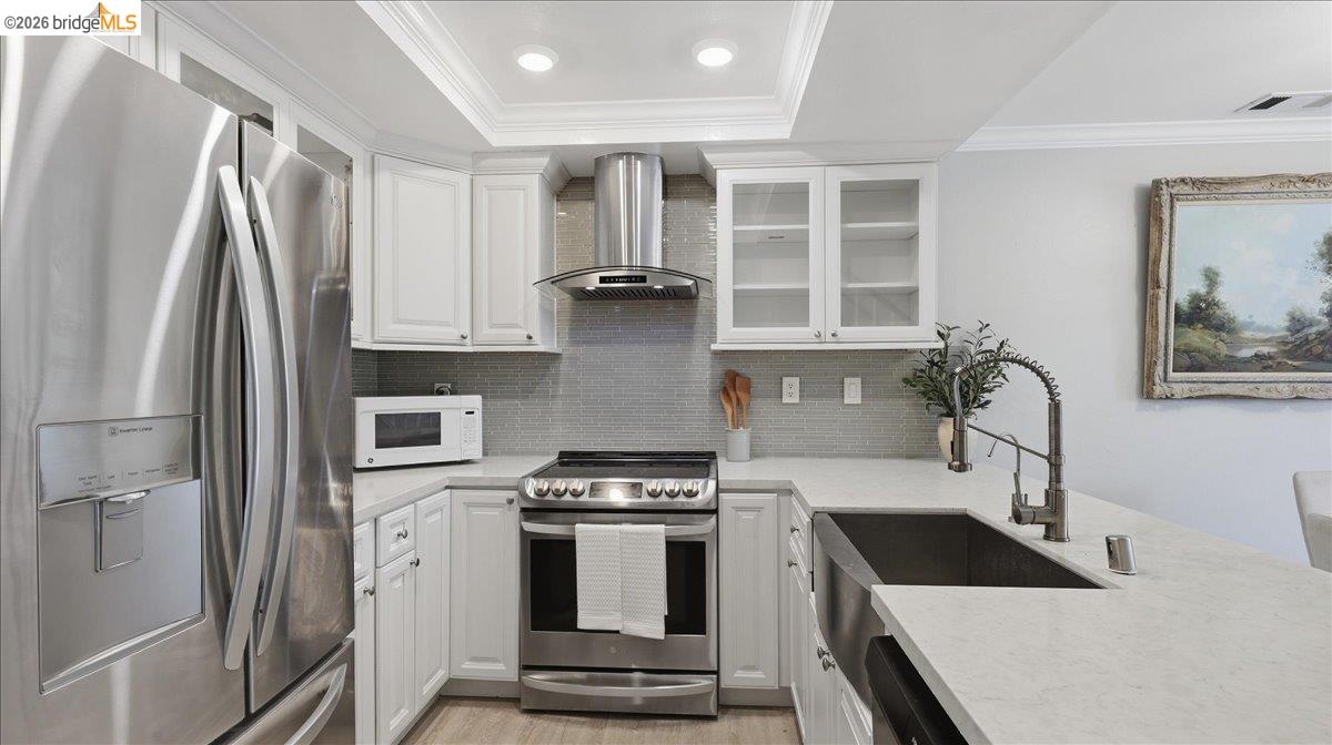 Kitchen with white cabinets, stainless steel appliances, gray tile backsplash, and a large farmhouse sink.