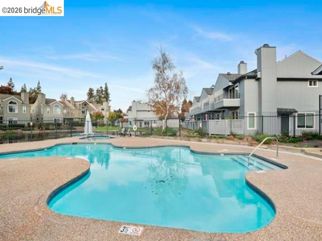 Outdoor swimming pool with a curved turquoise shape and fenced deck beside residential buildings.