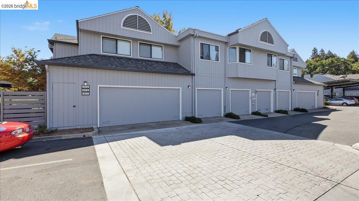 Gray two-story townhouse exterior with multiple garage doors and a paved parking area.
