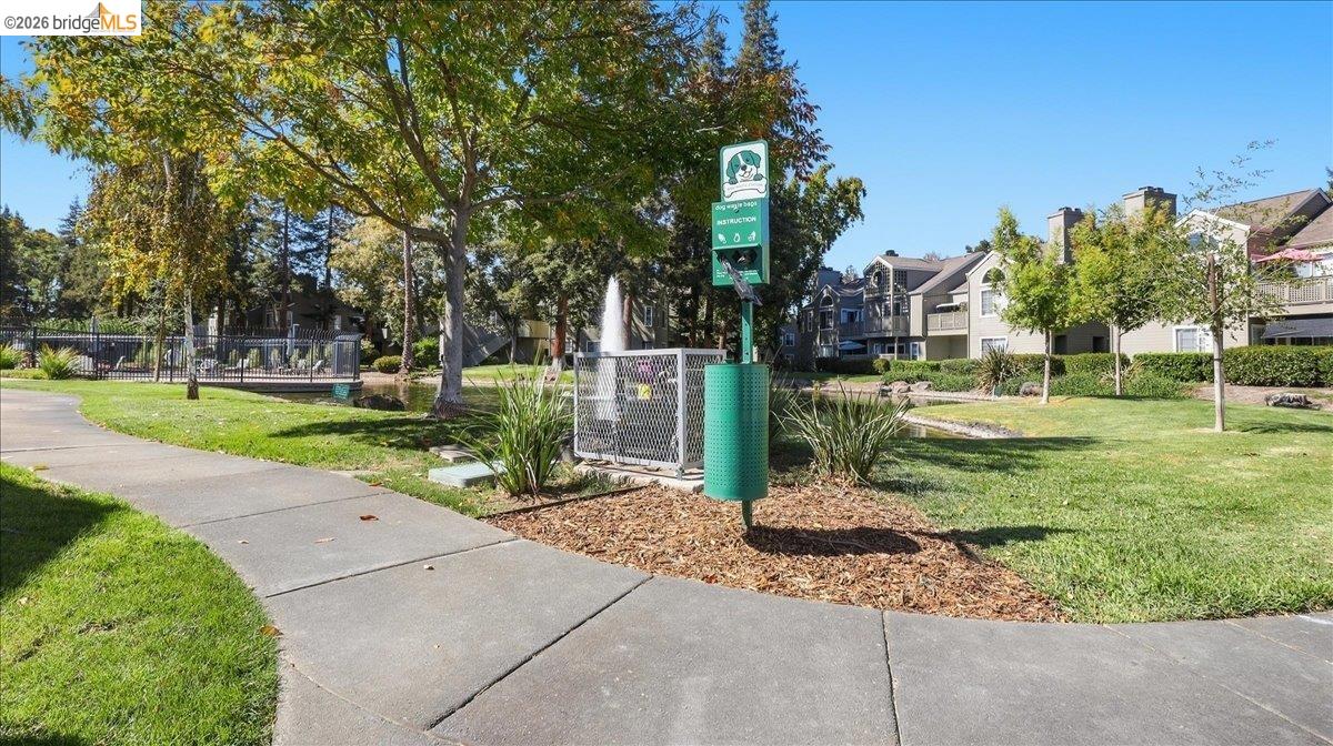 Community green space with a paved path, mature trees, dog-waste station, and fountain.