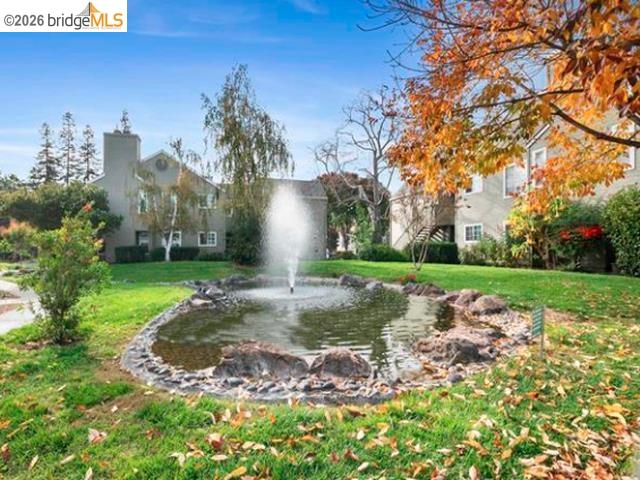 Residential courtyard with a rock-edged fountain pond and autumn trees in front of multi-unit homes.