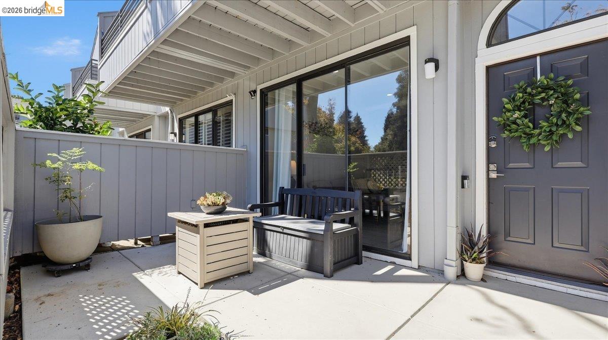 Private patio with a blue front door, sliding glass doors, and a bench beneath an upper balcony.