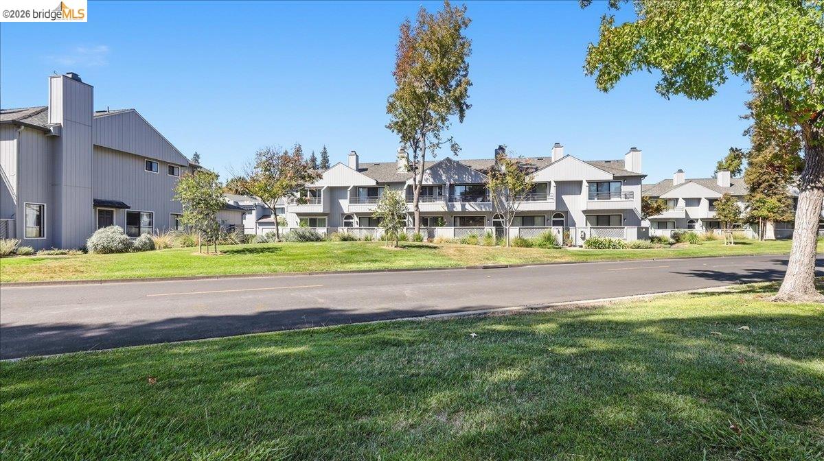 Gray multi-unit residences with balconies behind a broad lawn and tree-lined street.