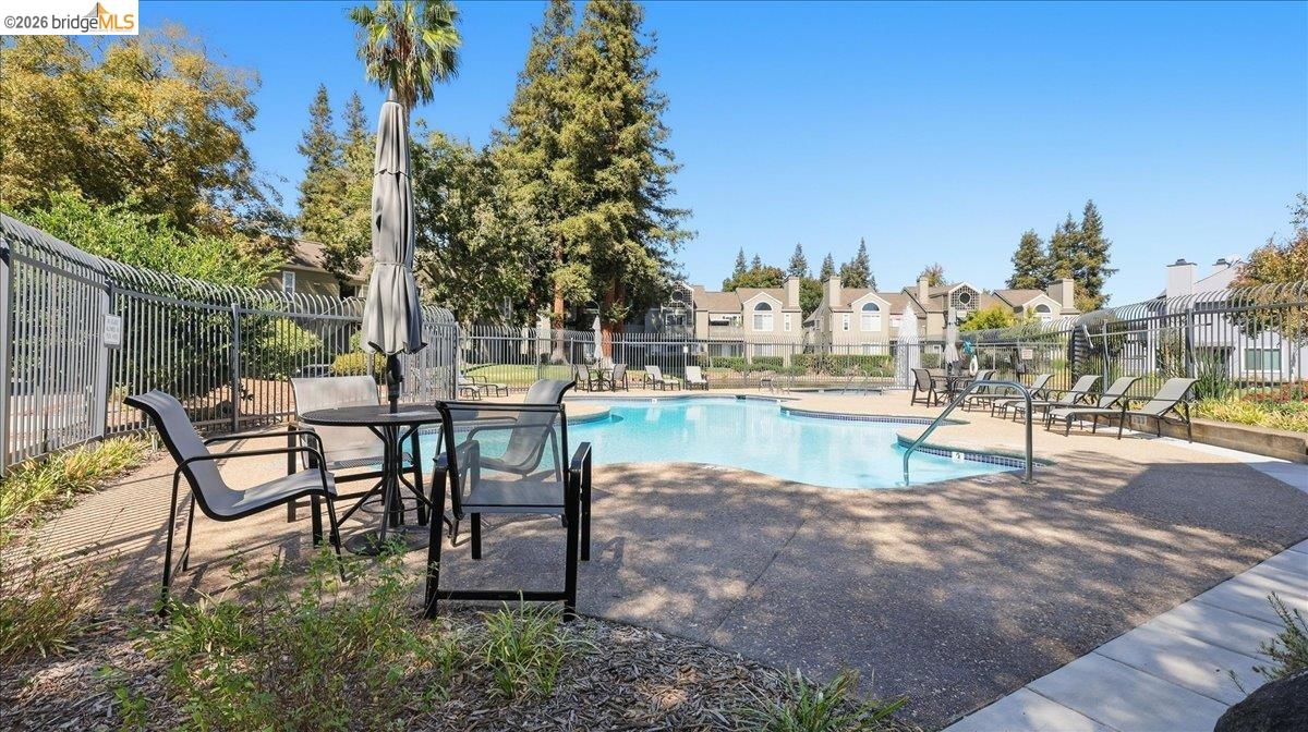 Community swimming pool with lounge chairs and patio tables inside a metal fence.