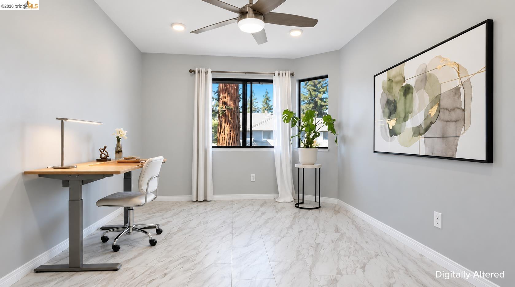 Staged home office with marble-look tile floors, a wood desk, and windows with white curtains.