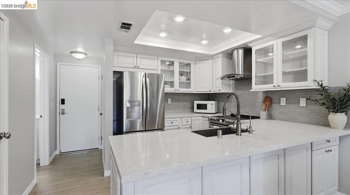 Bright white kitchen with a large island, black sink, gray tile backsplash, and stainless steel appliances.