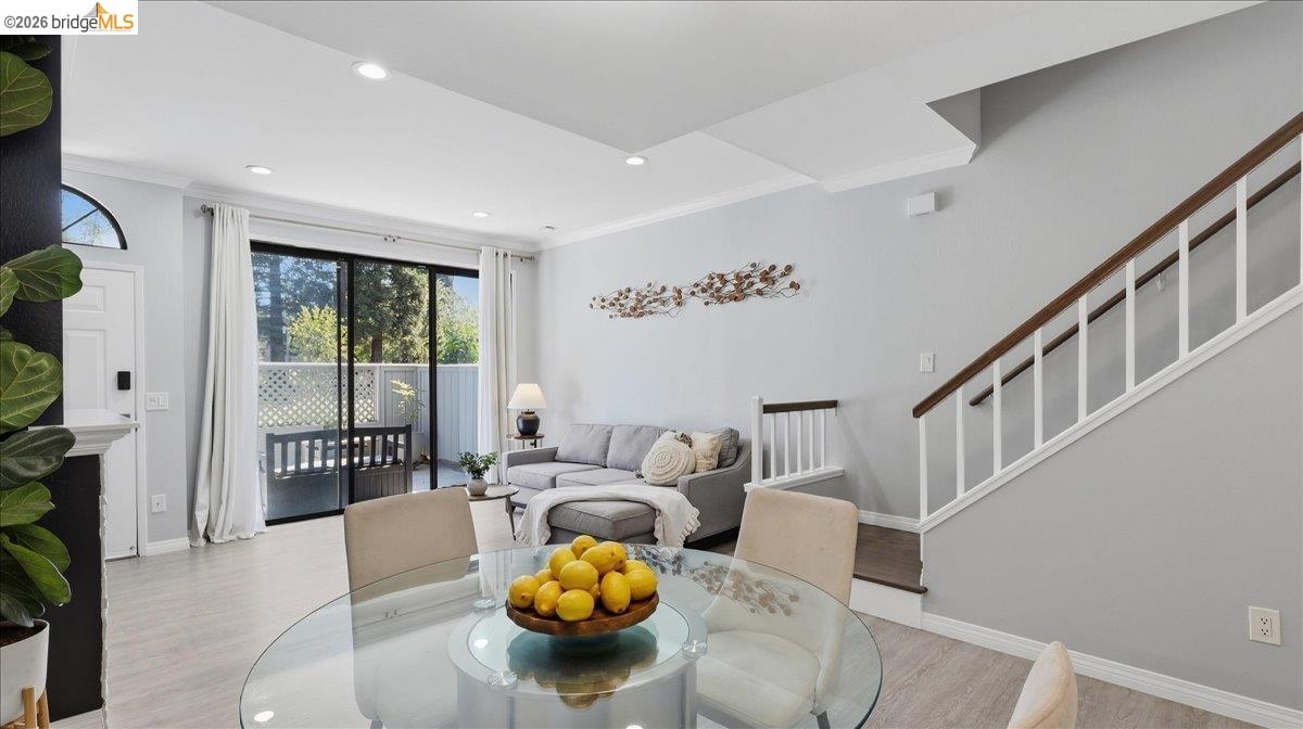 Living and dining area with a gray sectional, glass table, staircase, and sliding doors to a patio.
