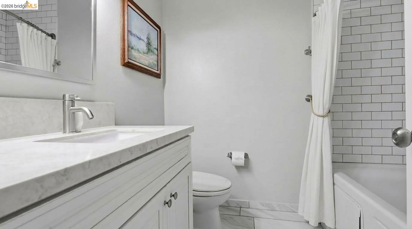 Bathroom with a white vanity, marble-look countertop, and subway-tile tub surround.