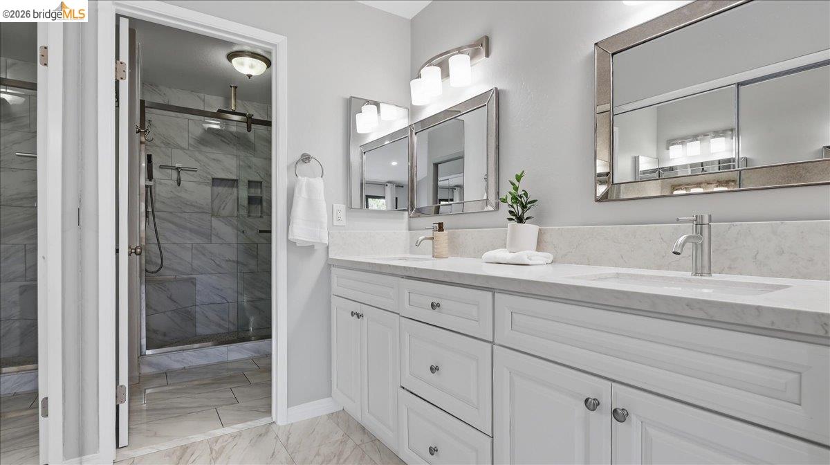Bright bathroom with a double-sink vanity and glass-enclosed marble-look shower.
