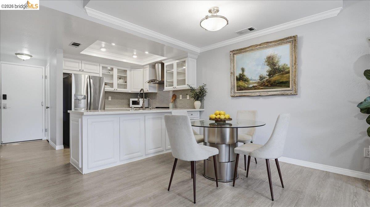White kitchen with stainless steel appliances beside a round glass dining table and upholstered chairs.