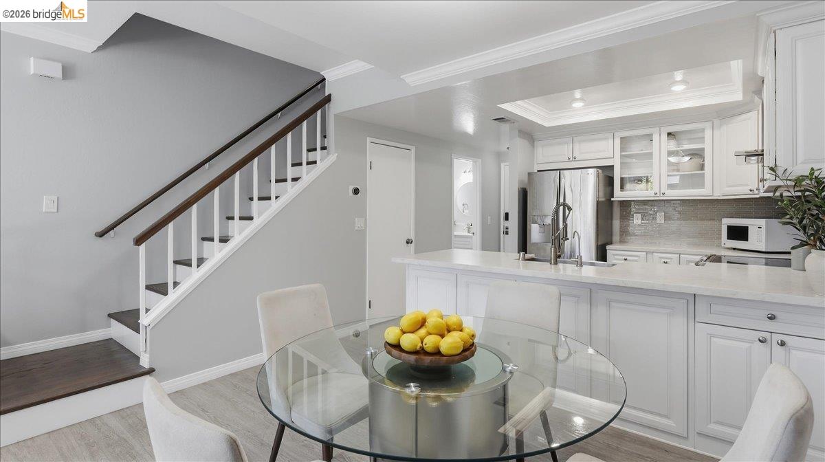 Bright kitchen with a large white island, glass dining table, and staircase with dark wood railing.