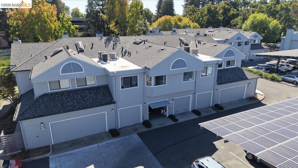 Aerial view of a gray multi-unit building with attached garages and a solar-panel parking canopy.