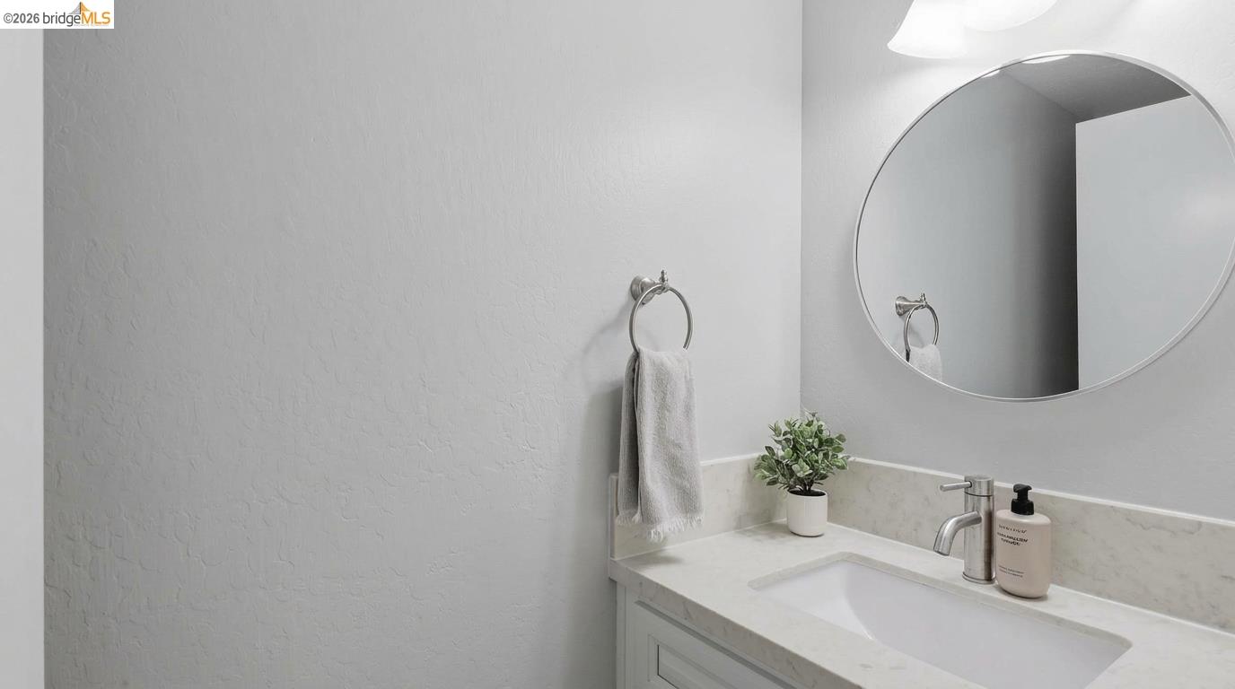 Bathroom vanity with a round mirror, marble-look counter, chrome faucet, and potted plant.