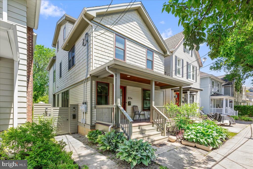 Two-story light-sided home with a covered porch, front steps, and leafy garden beds.