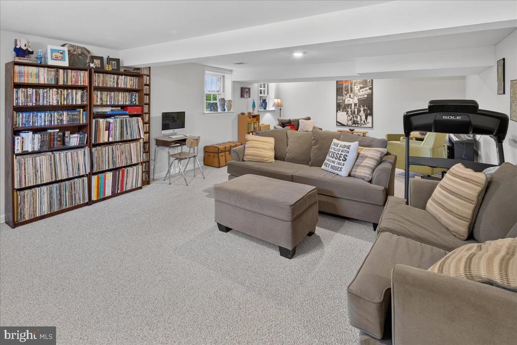 Furnished recreation room with media shelves, a sectional sofa, ottoman, and treadmill.
