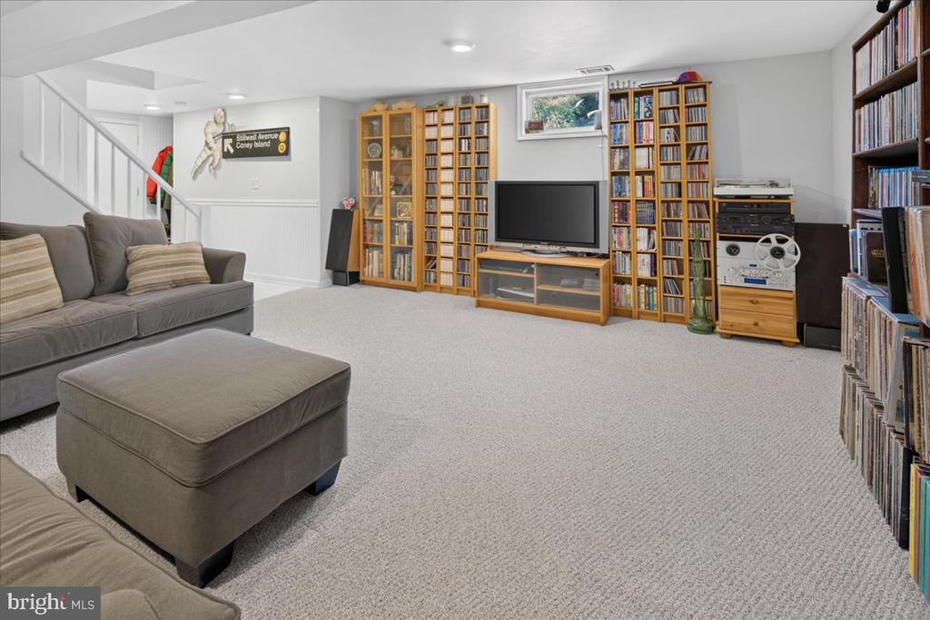 Basement family room with a gray sectional, ottoman, and wall of wooden bookshelves.