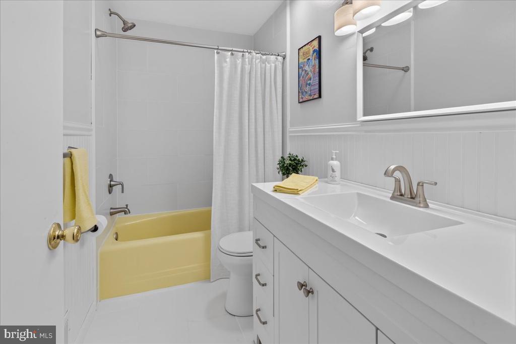 Bathroom with a yellow bathtub, white shower curtain, and long vanity with a single sink.
