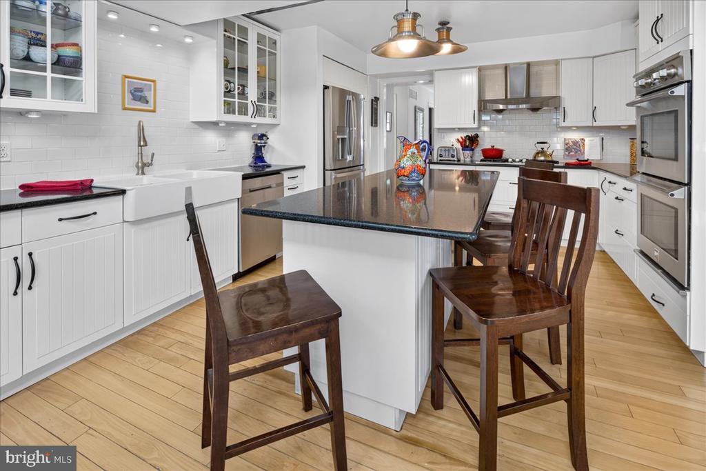 Bright white kitchen with a large dark stone island, bar seating, stainless steel appliances, and light wood floors.