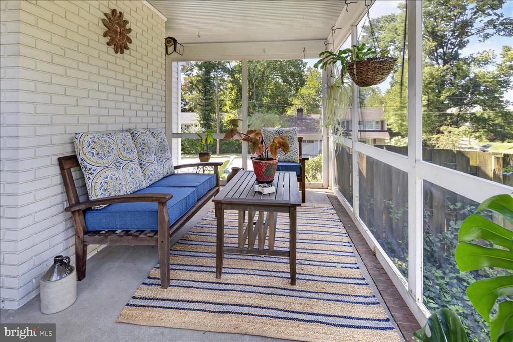 Enclosed porch with blue-cushioned seating, a striped rug, and screened windows overlooking trees.