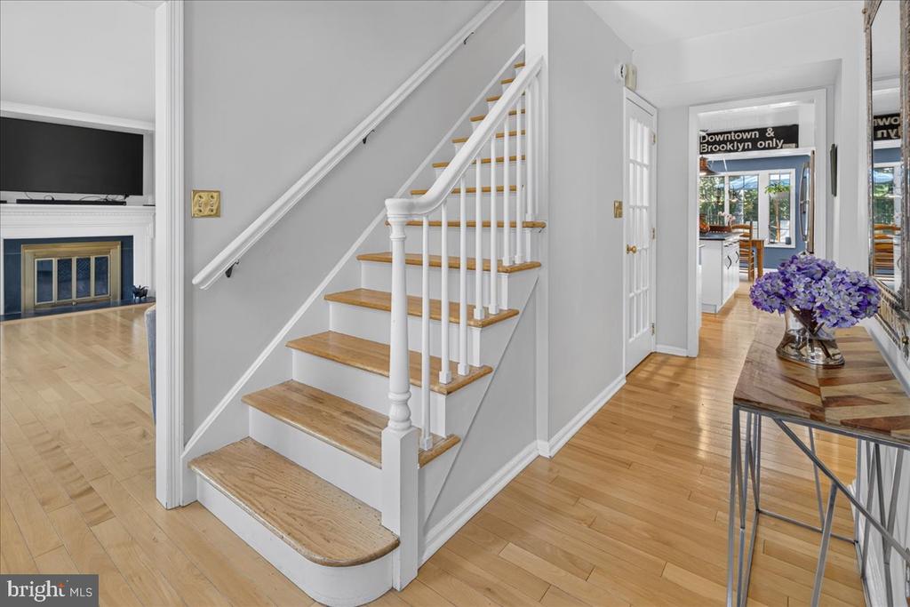 Foyer with a white staircase, wood treads, hardwood floors, and purple flowers on a console table.