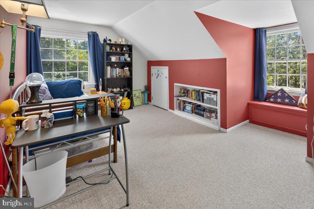 Attic bedroom with a desk, built-in book storage, and a red window seat beneath a window.