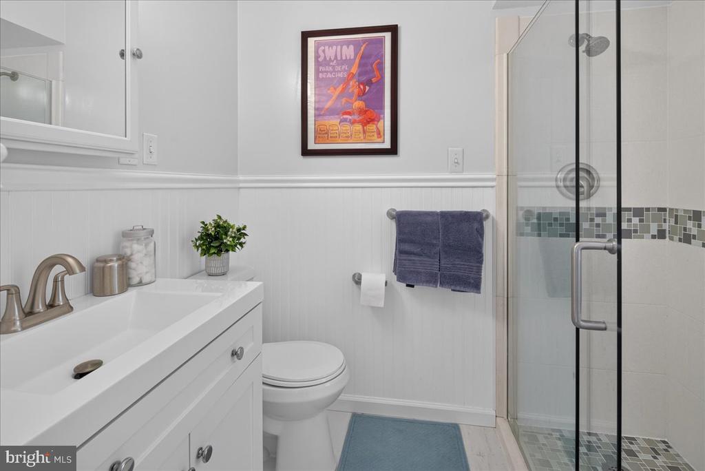 Bathroom with a white vanity, glass shower, mosaic tile accent band, and blue towels.