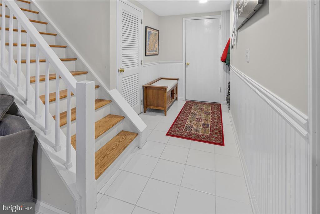 Entry hall with a white staircase, wood treads, tiled floor, and patterned red runner.