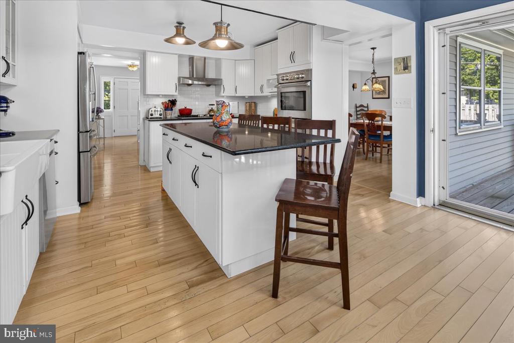Kitchen with a large dark-topped island, white cabinetry, stainless appliances, and hardwood floors.