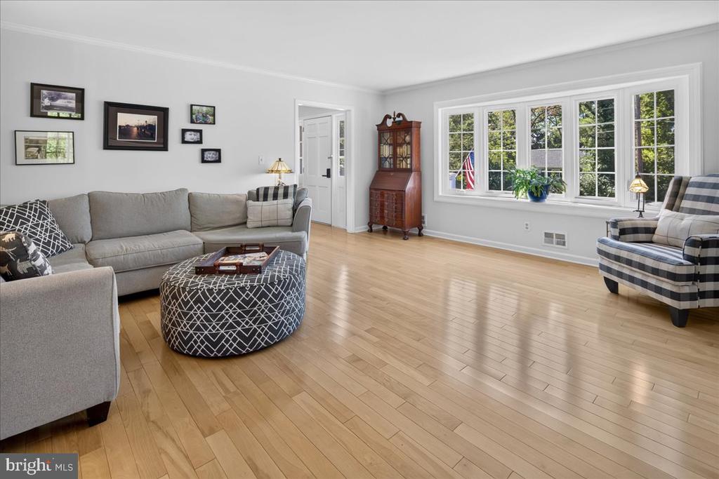 Furnished living room with a gray sectional, patterned ottoman, and large multi-pane windows.
