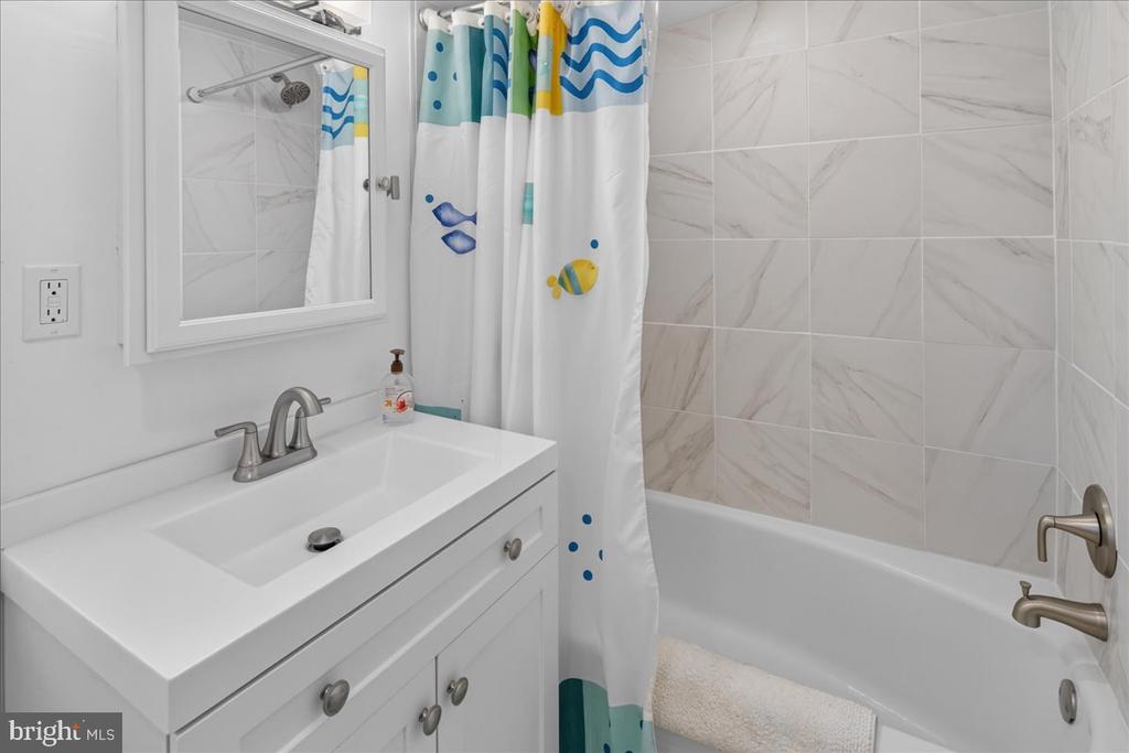 Bathroom with a white vanity, marble-look tile, and a colorful fish-print shower curtain.