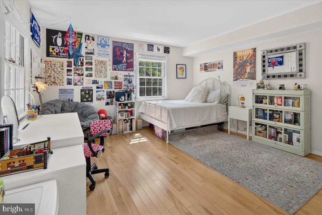 Bedroom with a white bed, music posters covering the walls, and a desk beside a sunlit window.