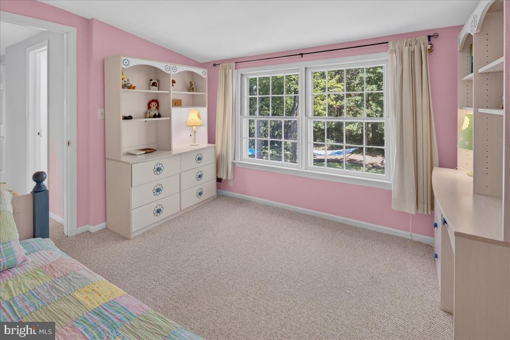 Pink bedroom with white built-in shelving and a wide window overlooking leafy greenery.
