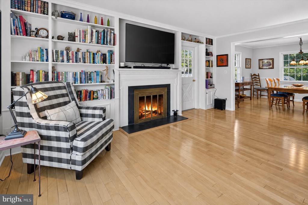 Living room with built-in bookshelves, a fireplace, and a plaid armchair beside the dining area.