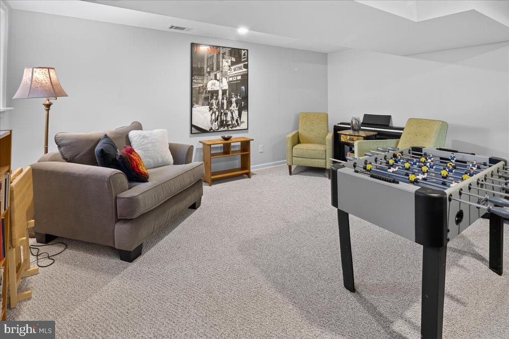 Furnished recreation room with a foosball table, sofa, armchairs, and digital piano.