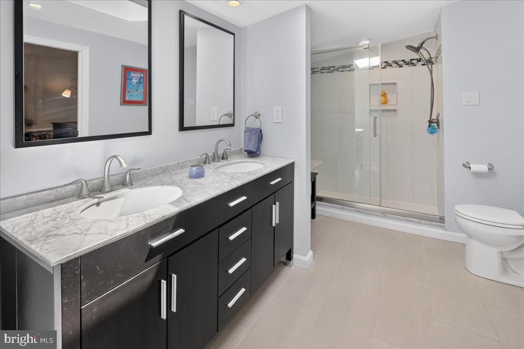 Bathroom with a dark double vanity, marble-look counter, and glass-enclosed tiled shower.