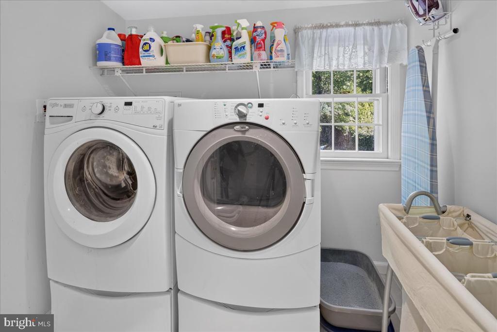 Laundry room with front-loading washer and dryer, supply shelf, and window.